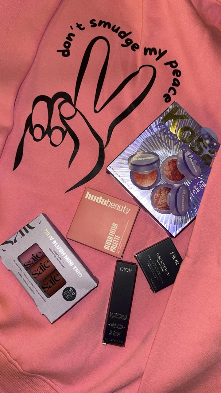 Makeup products and a pink sweatshirt with a peace sign design on a pink background